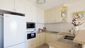 A kitchen with white cabinets, a built-in oven, a microwave, a sink, and a fruit bowl. - Bella Vista Shoal Bay (Shoal Bay)