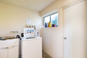 Une buanderie équipée d’un lave-linge, d’un évier et d’une fenêtre dont l’encadrement est orné de bouteilles.
