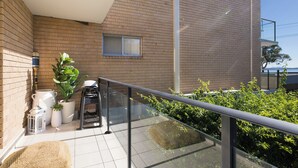 A balcony with a metal railing, a potted plant, a white outdoor table, and a window. - Bella Vista Shoal Bay (Shoal Bay)