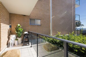 Ein Balkon mit Metallgeländer, einem Blumentopf, einem weißen Tisch für draußen und einem Fenster.