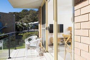 A balcony with a glass door, wicker furniture, and a view of neighboring houses. - Bella Vista Shoal Bay (Shoal Bay)