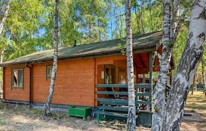 A wooden cabin with a porch, surrounded by trees.