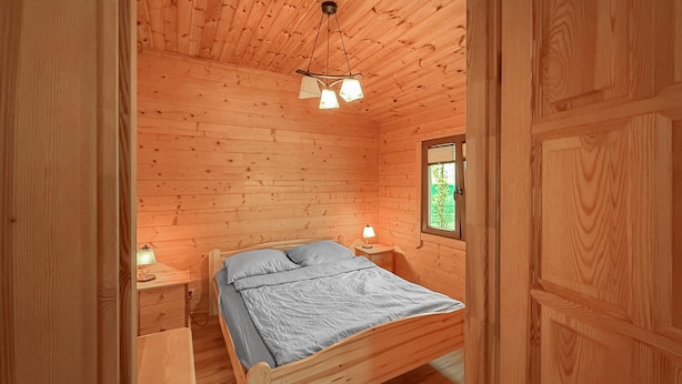 A wooden cabin bedroom with a single bed, bedside lamps, and a window with a view of greenery. - 2 bedroom gorgeous home in Dominikowo (Dominikowo)