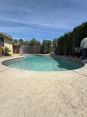 A backyard with a swimming pool, a wooden fence, and a basketball hoop. - 3-bedroom House w/private pool - Family & Pet Friendly (Sacramento)