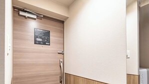 Entrada de una habitación de hotel con puerta de madera, un cartel con el plano de la habitación y suelo de baldosas.