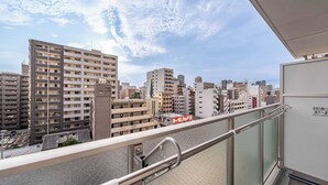 Un edificio alto con varios pisos, un balcón con barandilla metálica y un cielo despejado con algunas nubes.