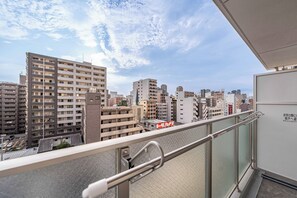 A high-rise building with multiple floors, a balcony with a metal railing, and a clear sky with scattered clouds. - Apartment Hotel 11 Dotonbori 10 (Osaka)