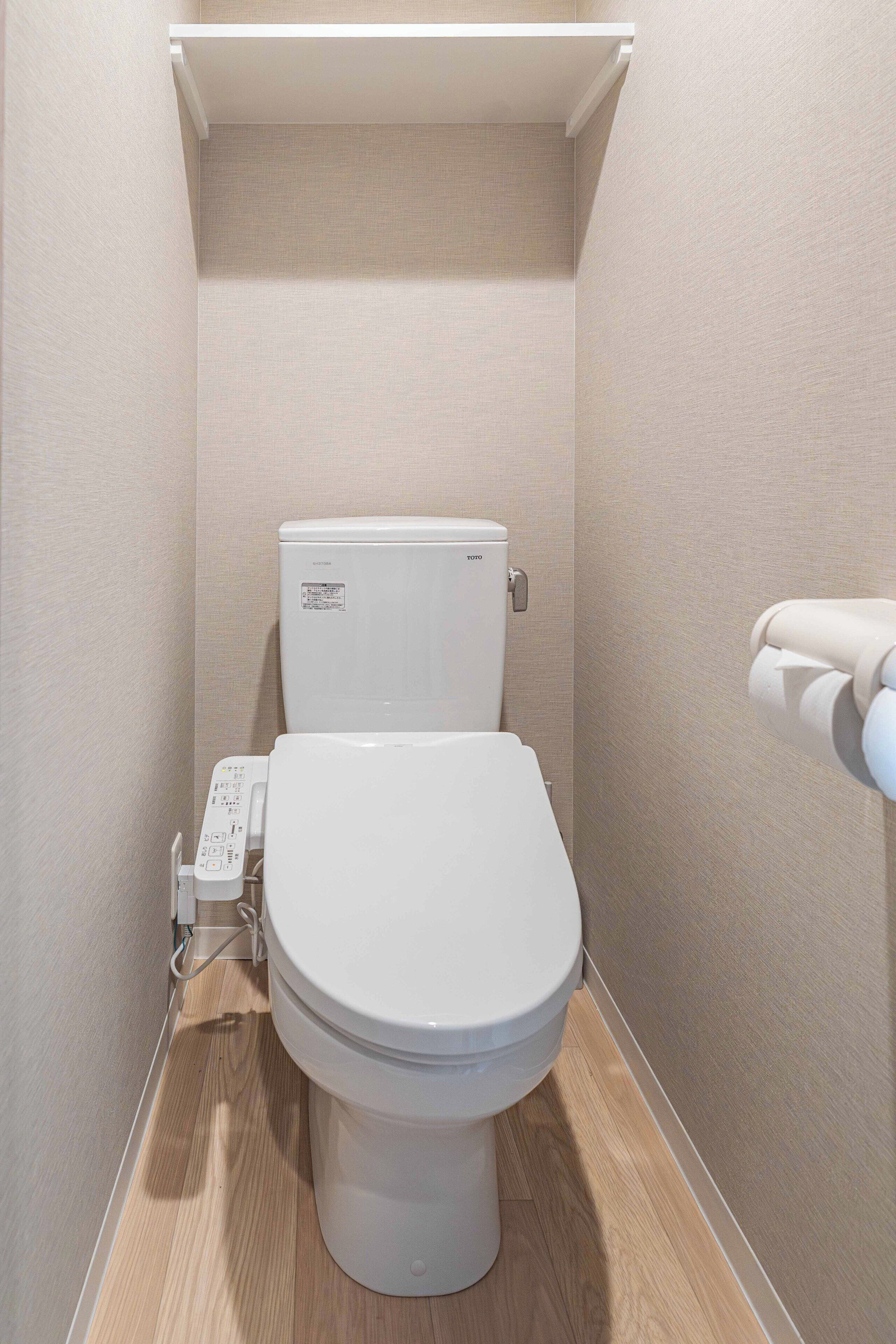 A compact, modern bathroom with a toilet, a wall-mounted bidet, and a toilet paper holder.