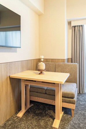 A corner room with a wooden table, a cushioned bench, a wall-mounted TV, and a window with curtains. - Apartment Hotel 11 Dotonbori 10 (Osaka)
