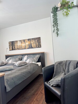 A bedroom with a bed, a chair, a wall-mounted plant, and a painting.