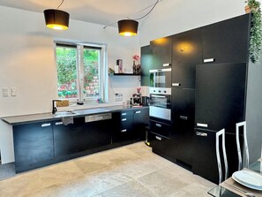 A modern kitchen with black cabinetry, stainless steel appliances, and pendant lighting.