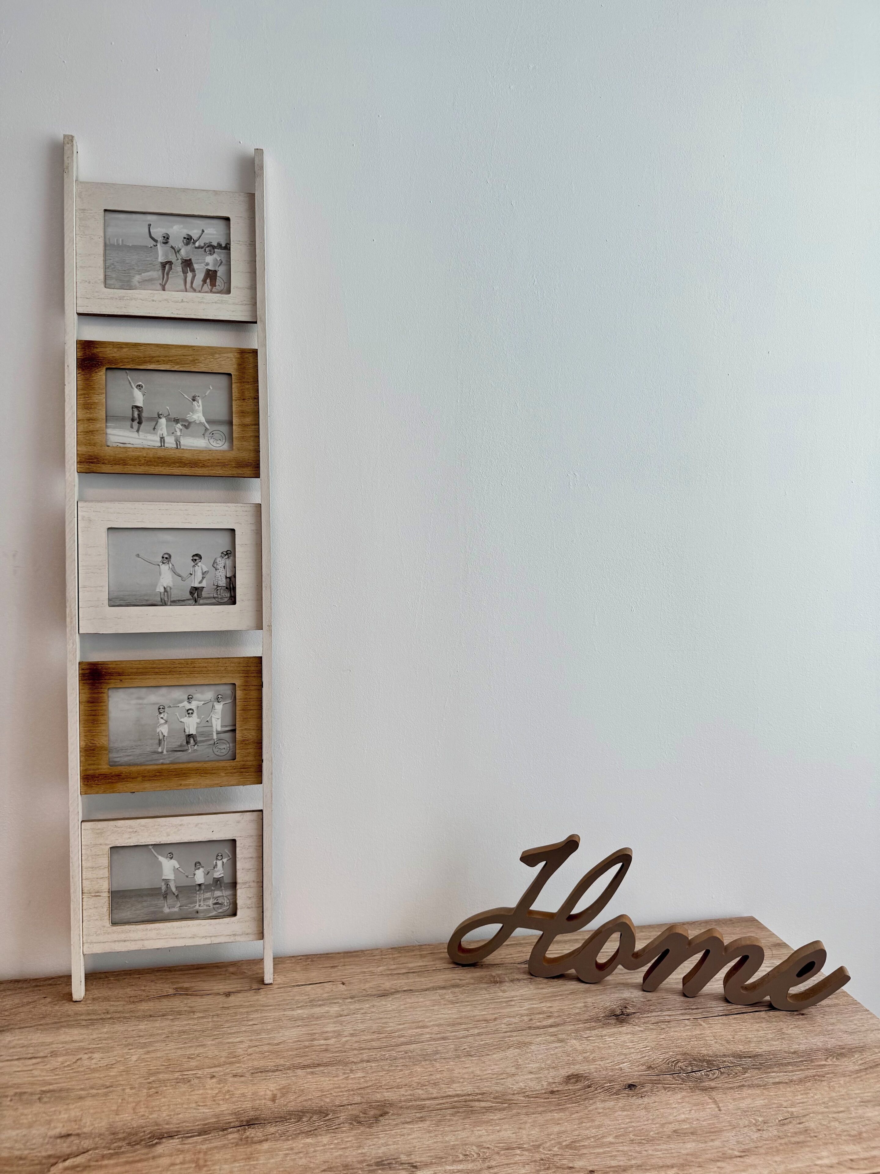 A wooden ladder with framed photographs against a wall, and a wooden sign with the word 'Home' on a wooden surface.