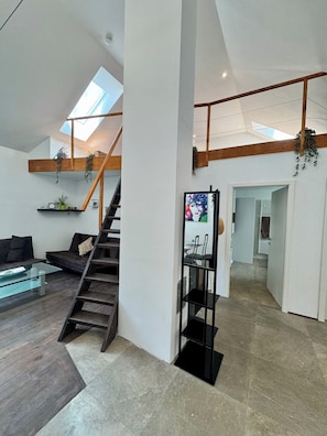 A modern interior with a staircase, a glass coffee table, and a black shelving unit.