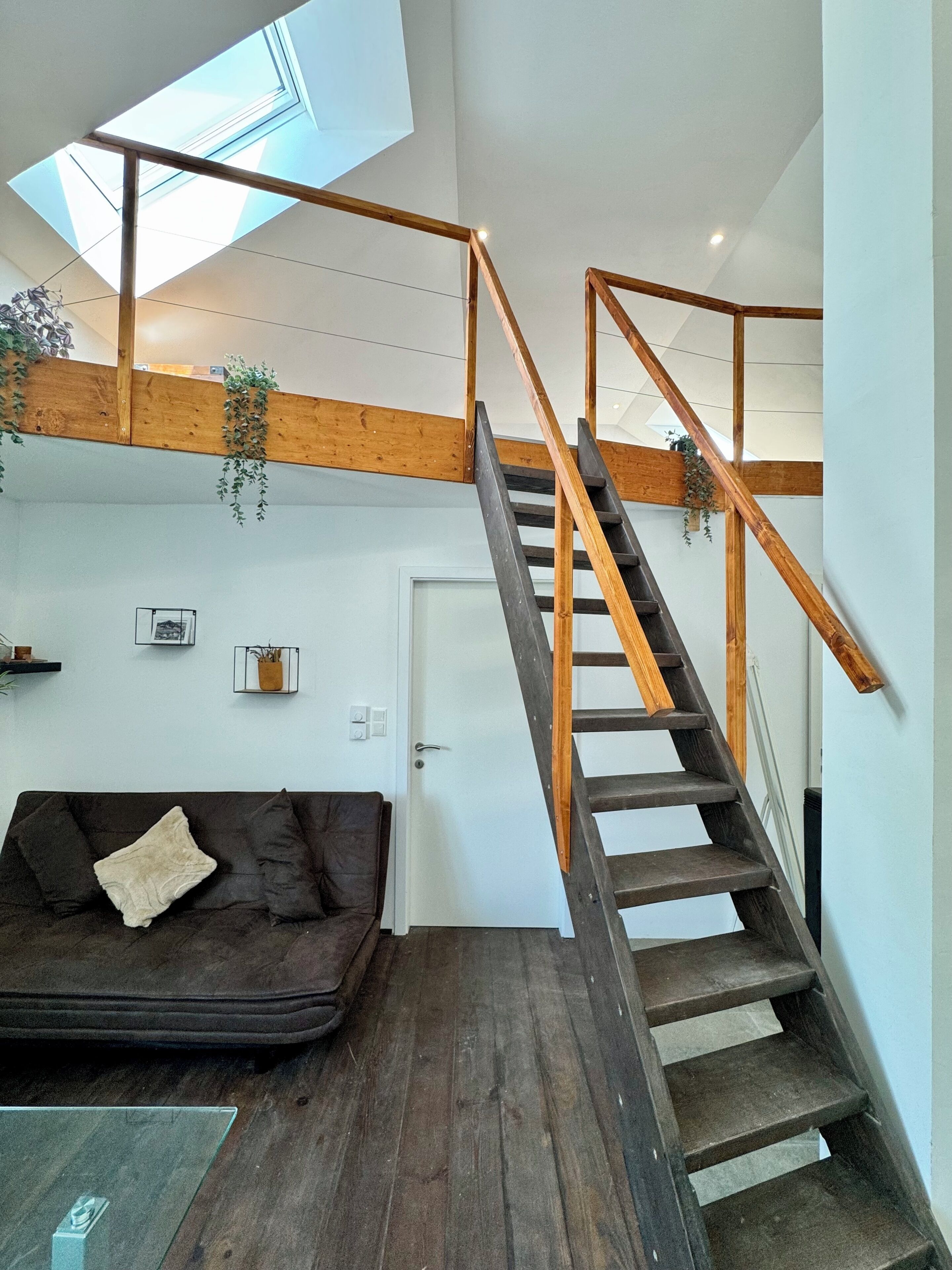 Un interior moderno con una escalera de madera, un sofá marrón oscuro y un tragaluz.