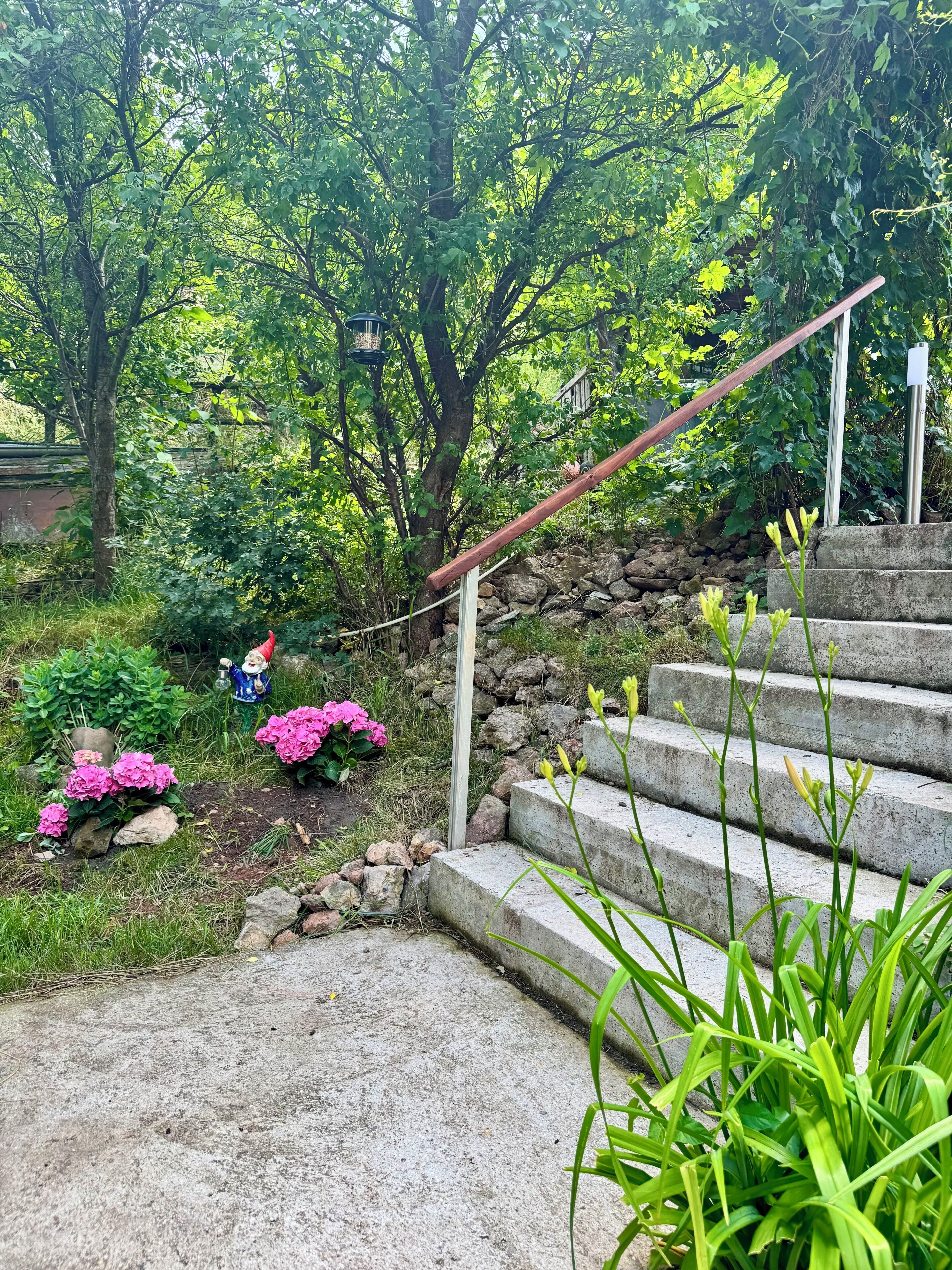 A garden with a stone staircase, a gnome statue, and pink flowers.