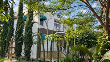 A courtyard with a fountain, lush greenery, and a building with a balcony.