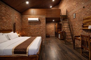 A room with a bed, a wooden ladder, a brick wall, and a wooden floor.