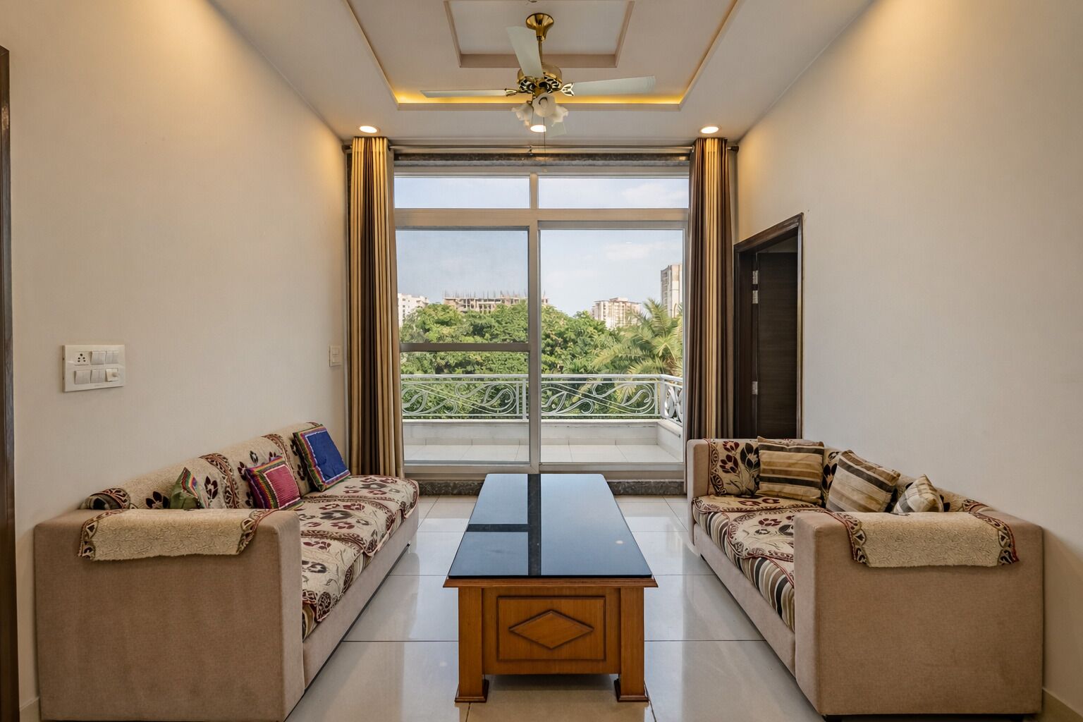 A room with two sofas facing a large window, a central table, and a ceiling fan.