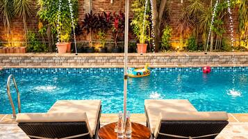 A poolside area with two lounge chairs, a table, and a red umbrella.