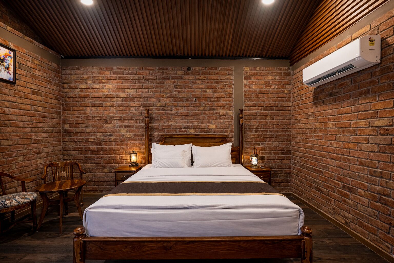 A room with a brick wall, a wooden bed, two bedside tables with lamps, and a chair.