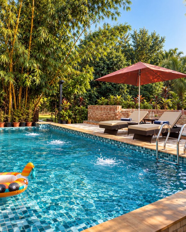 A swimming pool with lounge chairs and an umbrella, surrounded by lush greenery.