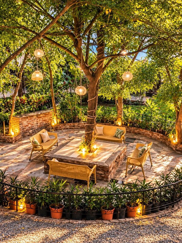 Un espacio al aire libre con mobiliario de mimbre, una mesa central y luces colgantes.
