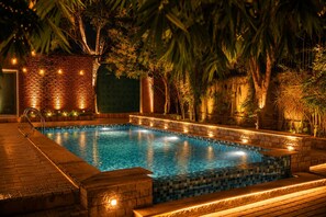 A swimming pool with tiled edges, surrounded by a brick wall and plants, with string lights along the top.
