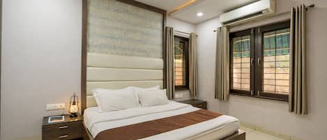 A bedroom with a bed, bedside tables, an air conditioning unit, a ceiling fan, and windows with curtains.
