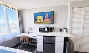A hotel room with a desk, a microwave, a coffee maker, a trash bin, a chair, and a window with curtains. - Waikiki 2BR 2BA 34th Fl Ocean View Sunset/Sunrise (Honolulu)