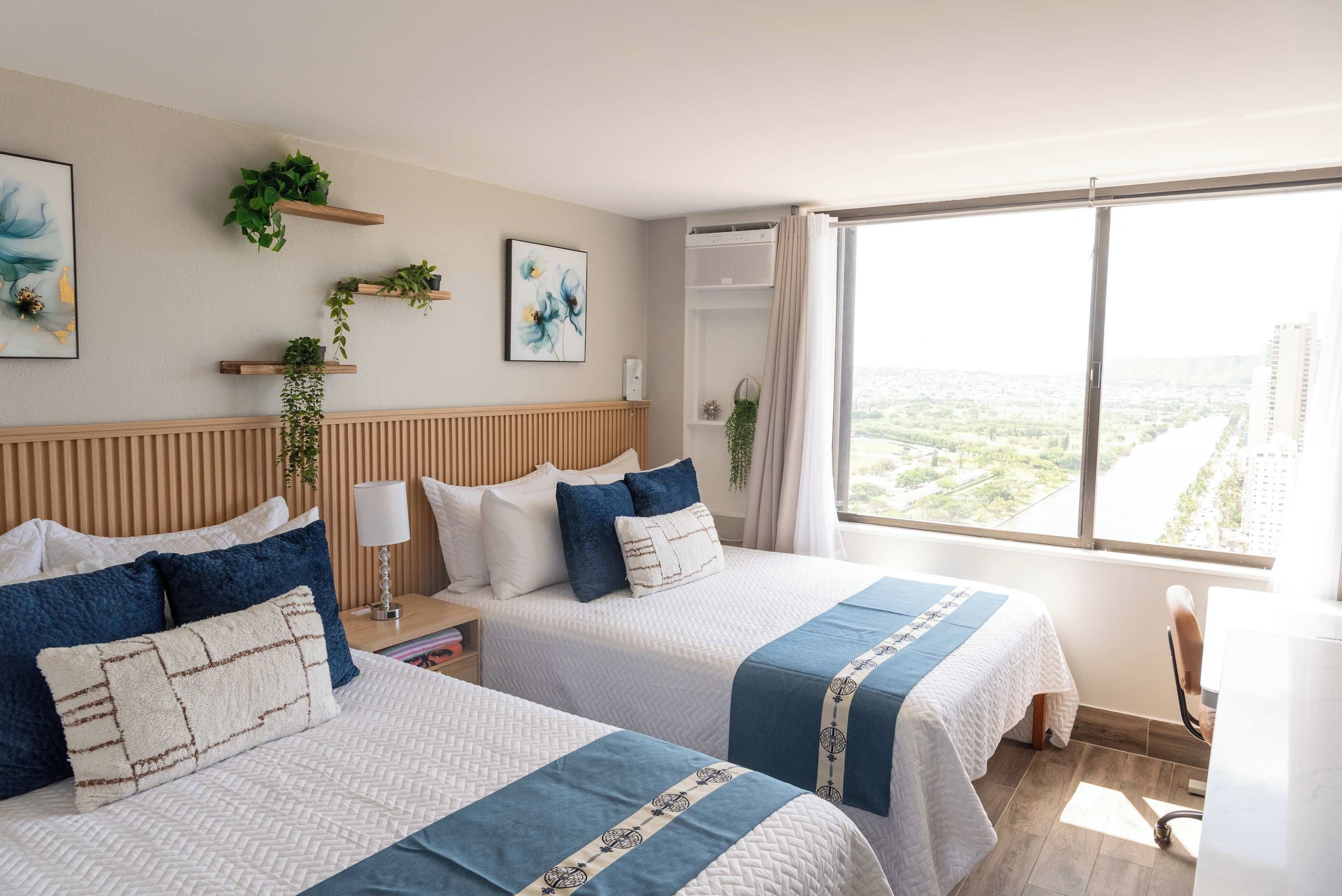 Habitación de hotel con dos camas, un ventanal grande y vistas a la ciudad.