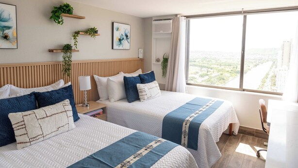 A hotel room with two beds, a large window, and a city view. - Waikiki 2BR 2BA 34th Fl Ocean View Sunset/Sunrise (Honolulu)