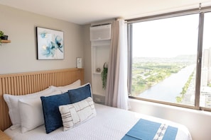 Een hotelkamer met een bed, een raam met uitzicht op de stad, een wandairconditioning en een kunstwerk aan de wand.