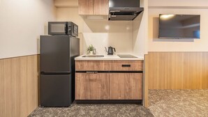 A compact kitchen with a refrigerator, microwave, sink, and wooden cabinets. - Apartment Hotel 11 Hanazono 1 (Osaka-shi)