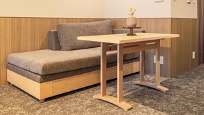A room with a sofa, a small wooden table, and a vase with flowers. - Apartment Hotel 11 Hanazono 1 (Osaka-shi)