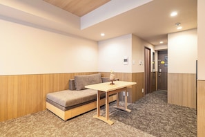 A small, cozy room with a sofa, a table, and a door. - Apartment Hotel 11 Hanazono 1 (Osaka-shi)