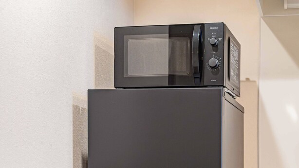 A black refrigerator with a microwave on top, situated next to a wooden cabinet and a white countertop. - Apartment Hotel 11 Hanazono 1 (Osaka-shi)