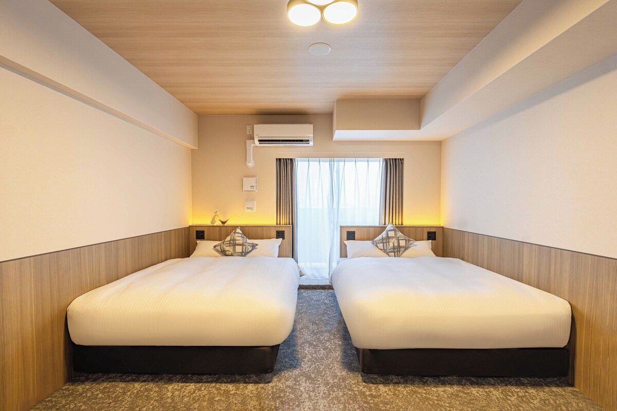 Ein Hotelzimmer mit zwei Betten, einer Klimaanlage, einem Fenster mit Vorhängen und einer Deckenleuchte.