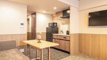 A compact kitchen with a microwave, refrigerator, and a small dining area with a table and bench.