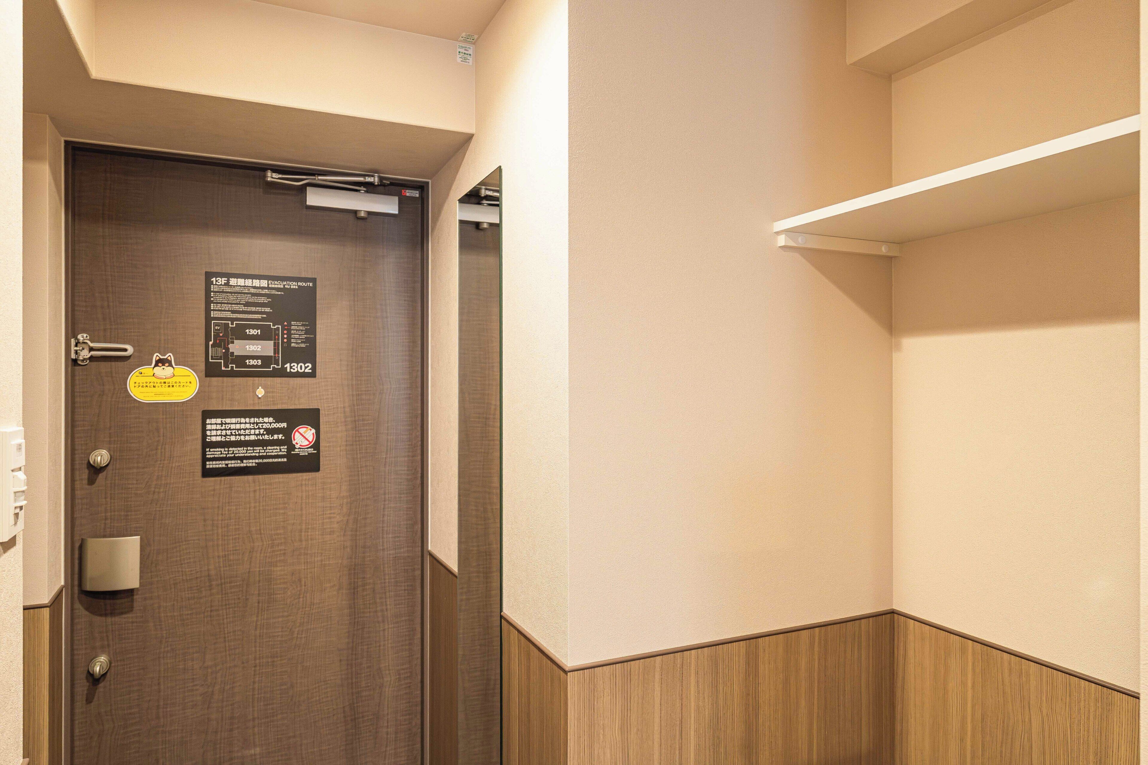 Habitación de hotel con una puerta de madera, una repisa montada en la pared y un cartel que indica una ruta de evacuación.