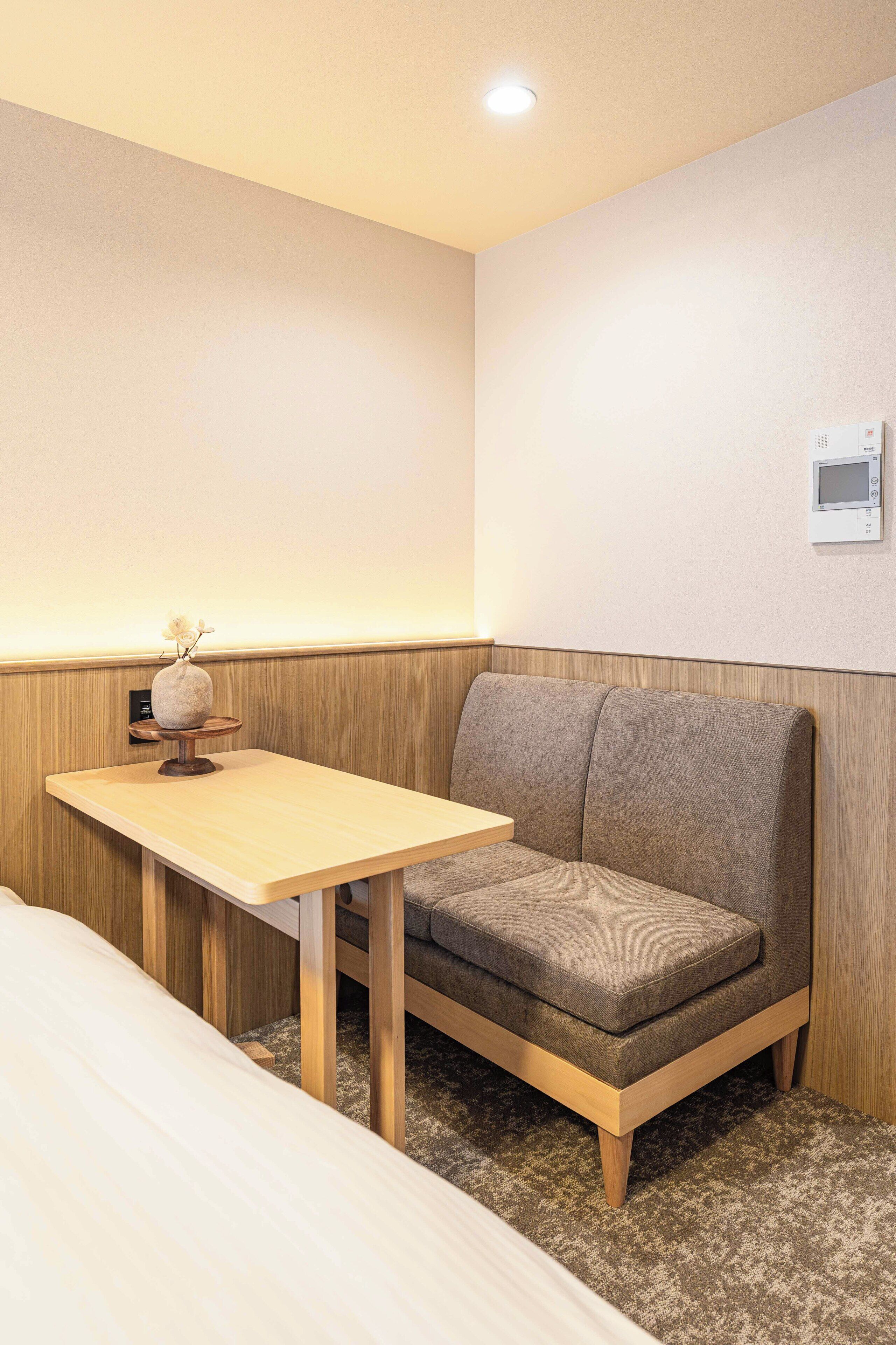 A small, cozy room with a wooden table and bench, a vase with flowers, and a wall-mounted device.