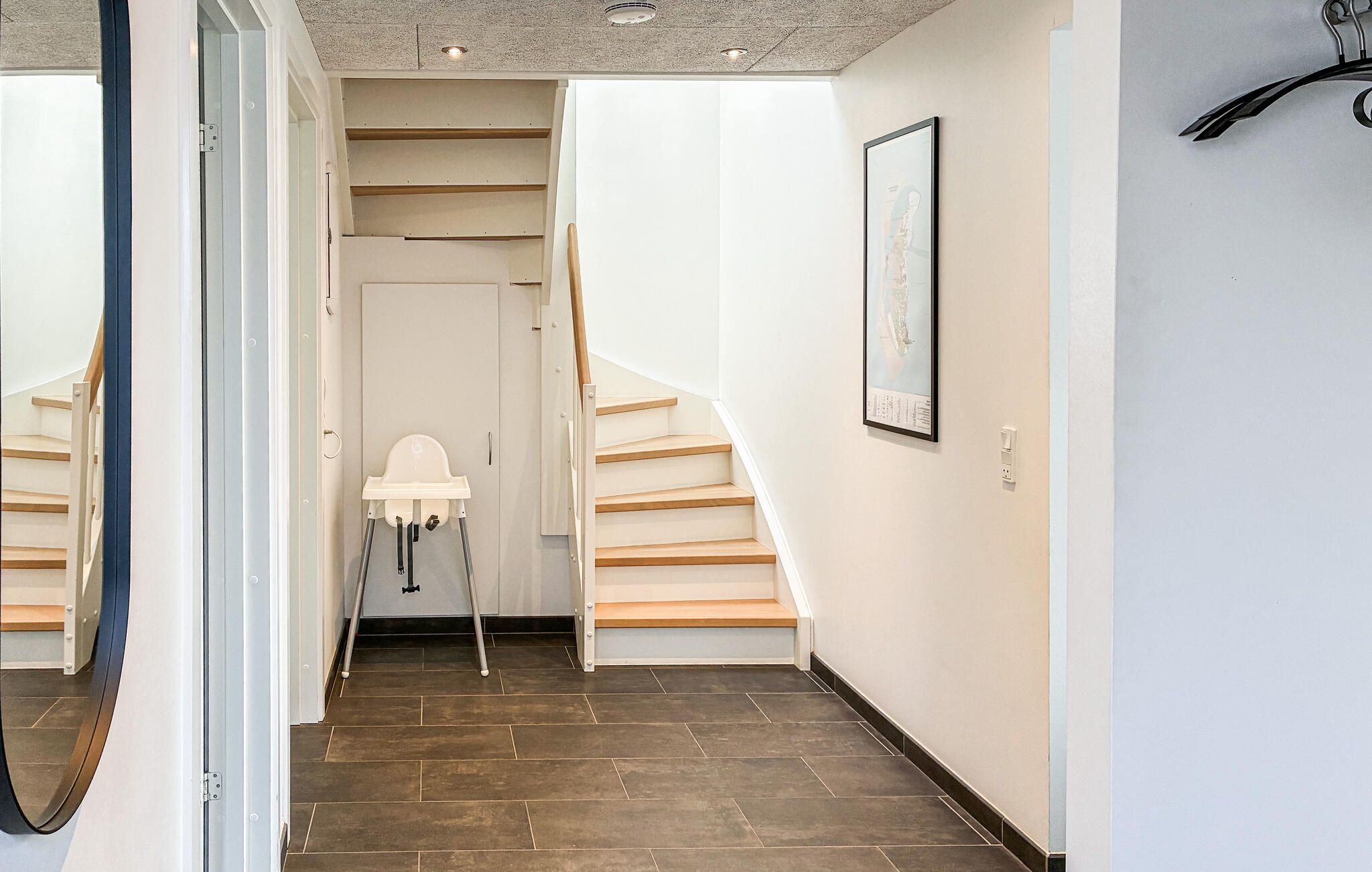 A hallway with a staircase, a white baby changing station, and a framed picture on the wall.