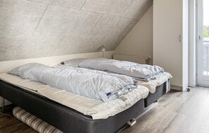 Een slaapkamer met een schuine kap, een bed met gestreepte beddengoed, een bedlampje en een uitzicht op de buitenwereld door een deur.