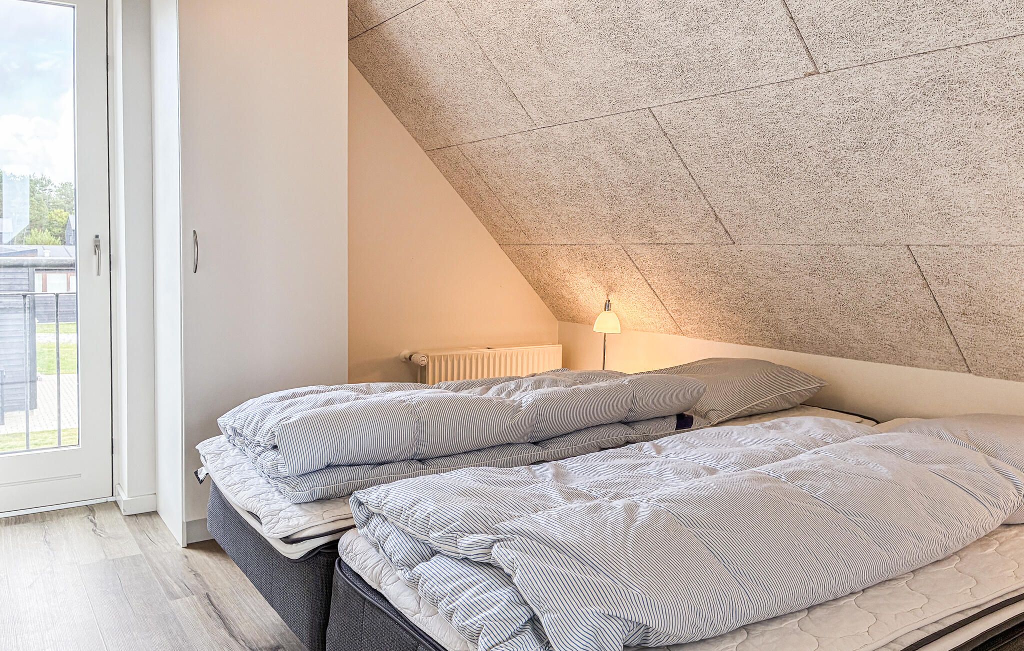 Une chambre avec deux lits, un radiateur, une lampe et un plafond en pente.