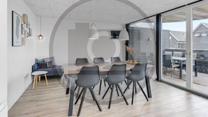 Uma sala de jantar moderna com divisória de vidro, um sofá e uma mesa de jantar com cadeiras.