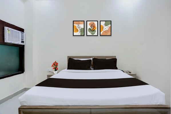 Habitación de hotel con cama, mesita de noche, televisor montado en la pared y tres cuadros enmarcados sobre la cama.