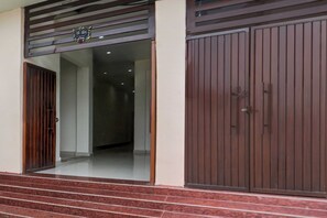 A building entrance with a set of stairs leading up to a door, a large brown door with a metal handle, and a small decorative emblem above the door. - Super OYO Collection O Kalyanpur Metro (Kanpur)