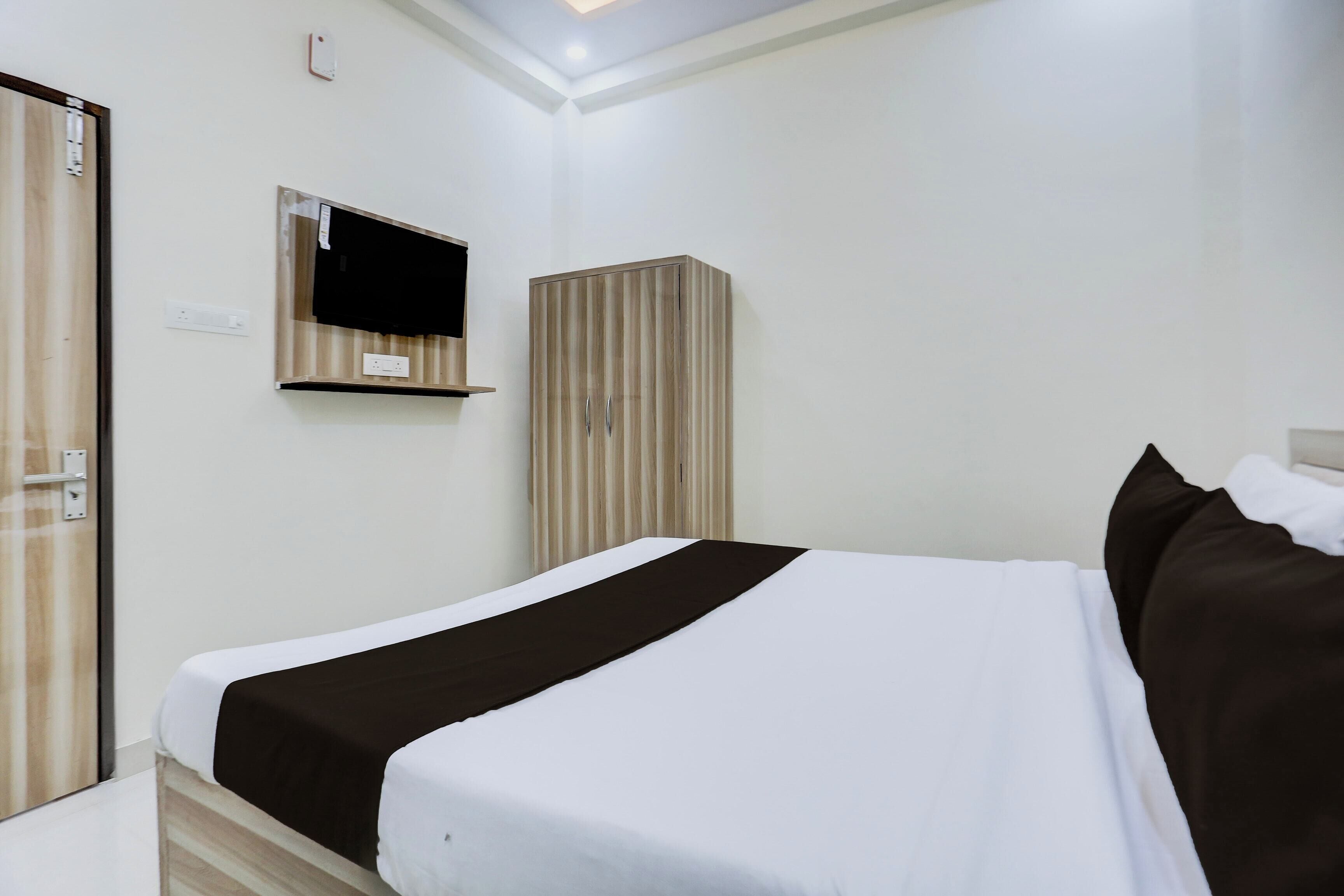 Una habitación de hotel con cama, armario, televisor montado en la pared y toma de corriente.