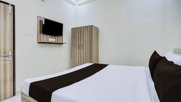 Una habitación de hotel con cama, armario, televisor montado en la pared y toma de corriente.