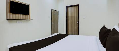 A hotel room with a bed, a television mounted on the wall, and two doors.