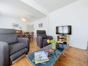 A modern living room with a sofa, armchair, and a coffee table with magazines and a vase of flowers. - Claire Joie by Interhome (Saint Brevin les Pins)